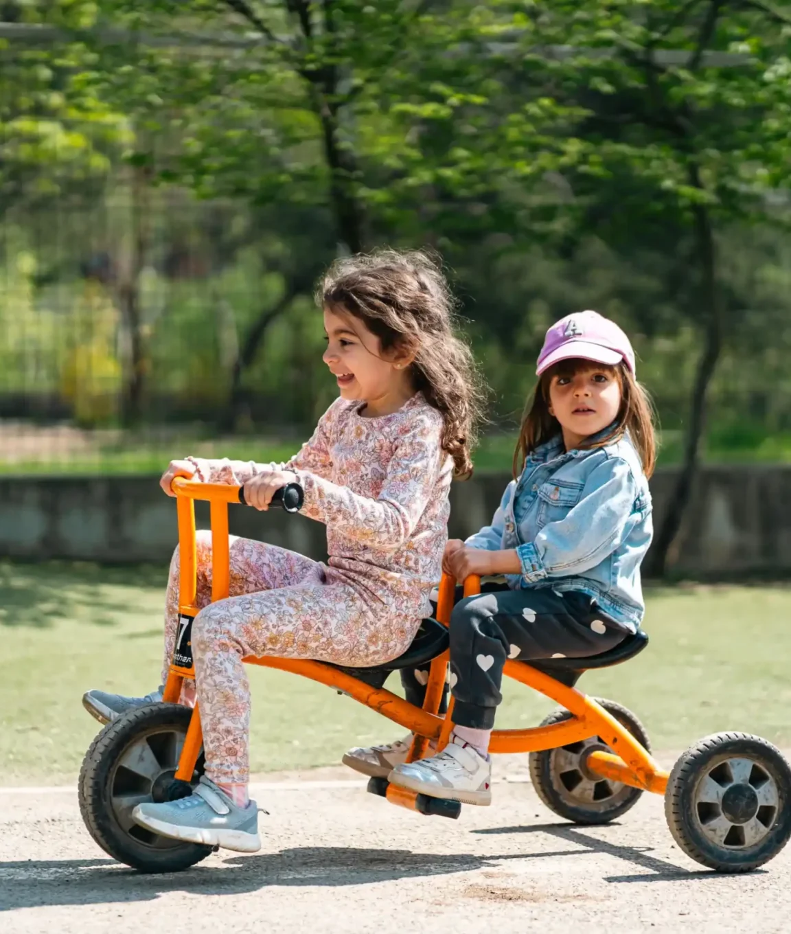 Deux enfants de maternelle partagent un tricycle dans la cour