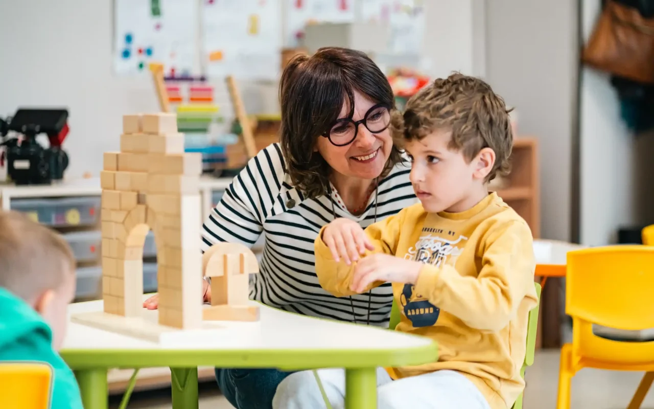 Une enseignante accompagne un élève de maternelle dans un atelier de construction